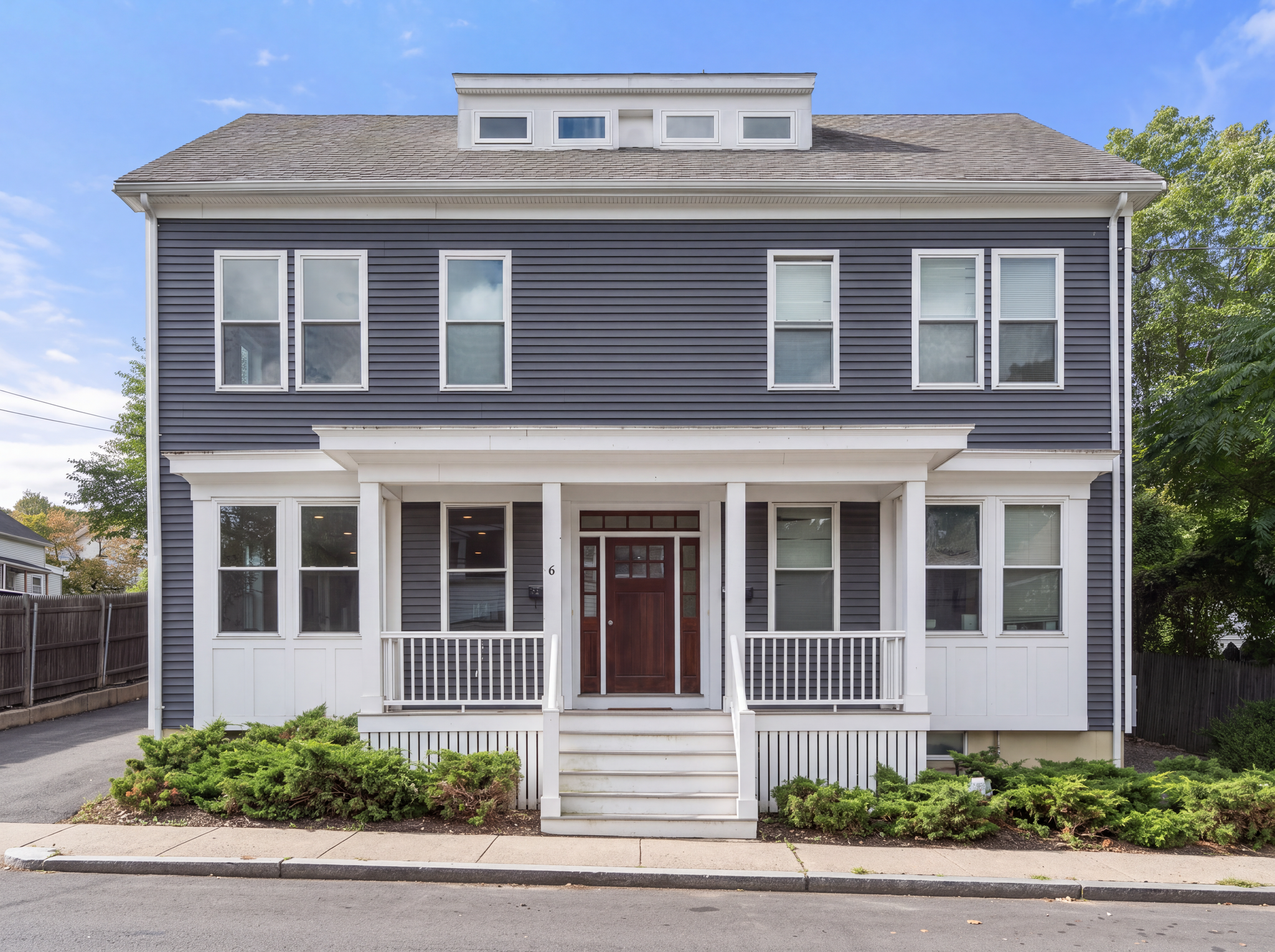 A two-story dark grey house with white trim features a prominent front porch, white railings, and a dark wooden door.
